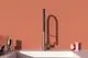 Küchenarmatur von Ideal Standard mit einem modernen Design. Der Wasserhahn steht vor einer einfarbigen Wand und einem weißen Becken. Farbige Gegenstände sind in der Nähe platziert.